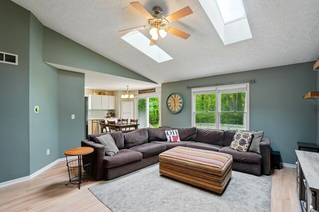 6963 Weurful Dr, Canal Winchester, OH 43110 - living room featuring a skylight, vaulted ceiling, a textured ceiling, light wood-type flooring, and a chandelier
