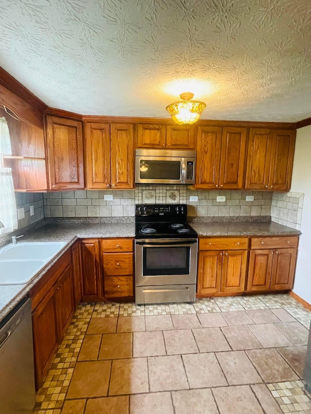 1275 Hathersage Pl, Galloway, OH 43119 - kitchen with appliances with stainless steel finishes, a sink, decorative backsplash, and brown cabinets