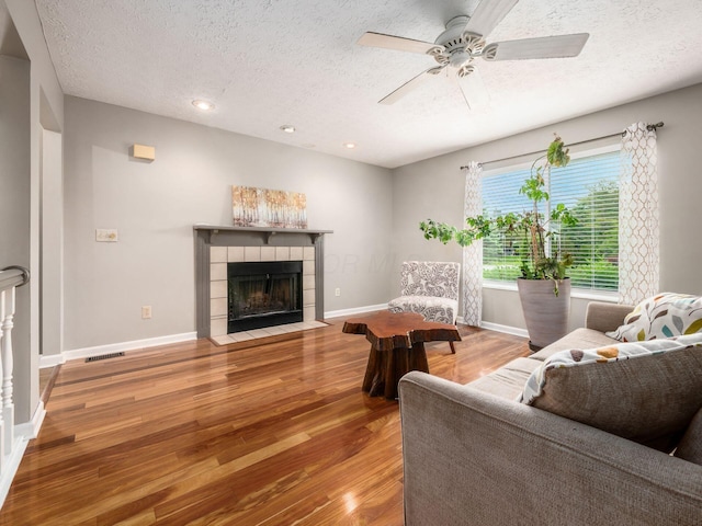 7020 Avery Rd, Dublin, OH 43017 - living room with a textured ceiling, wood finished floors, a ceiling fan, a tiled fireplace, and baseboards