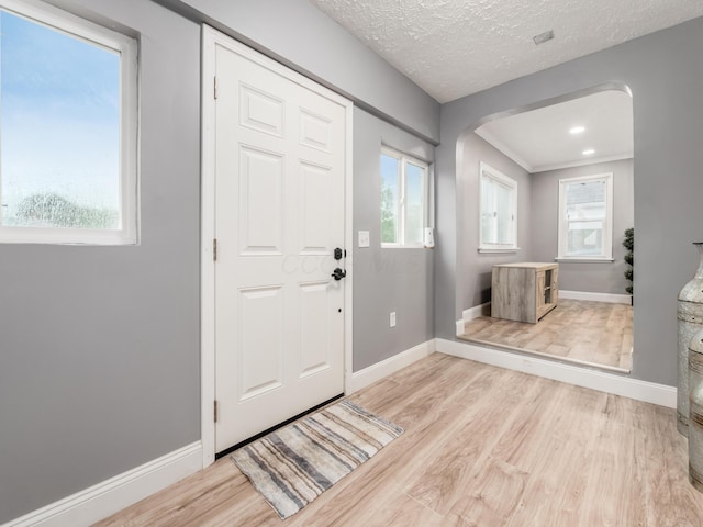 entryway featuring arched walkways, baseboards, wood finished floors, and healthy amount of natural light