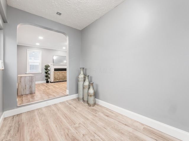 unfurnished room featuring arched walkways, wood finished floors, baseboards, recessed lighting, and a textured ceiling