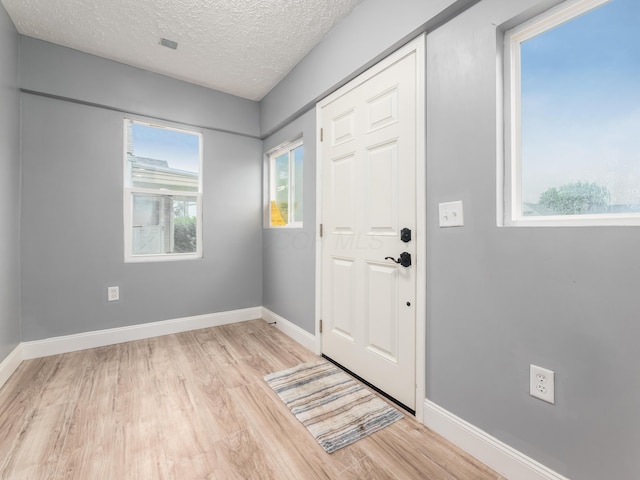 foyer with light wood finished floors, a textured ceiling, and baseboards