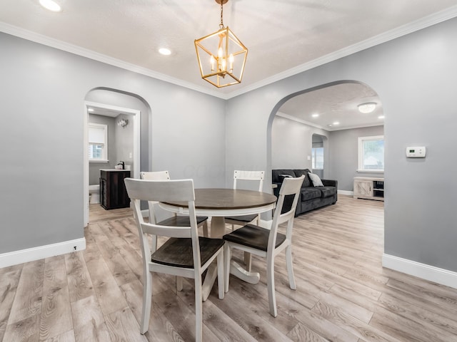 dining room with arched walkways, light wood-style flooring, baseboards, a chandelier, and ornamental molding