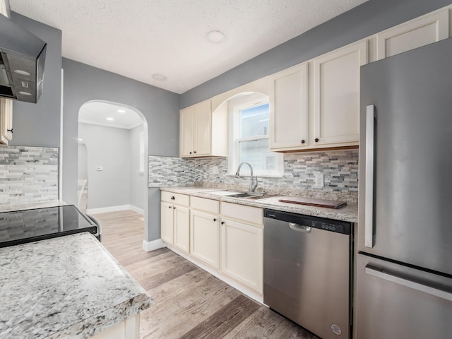 kitchen with stainless steel appliances, arched walkways, light countertops, a sink, and a textured ceiling