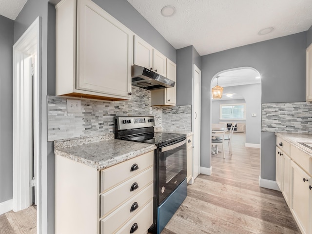 kitchen featuring stainless steel electric range, under cabinet range hood, arched walkways, light wood-style floors, and tasteful backsplash