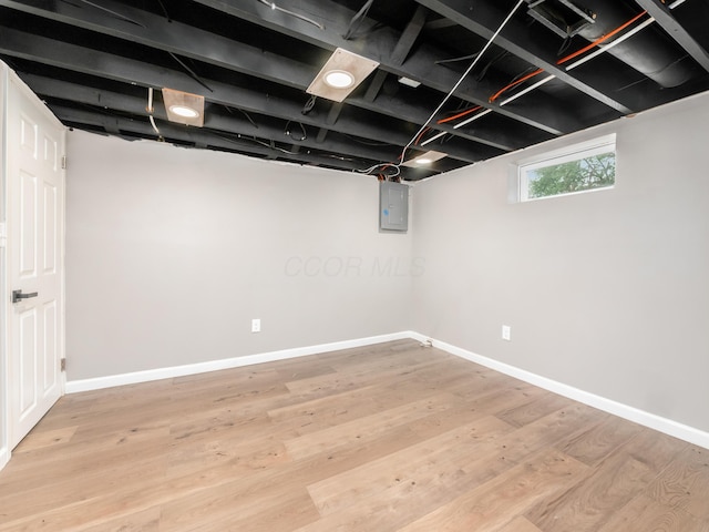 basement featuring electric panel, baseboards, and light wood-type flooring