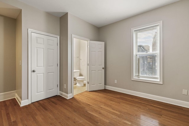 unfurnished bedroom with wood finished floors, baseboards, and ensuite bathroom