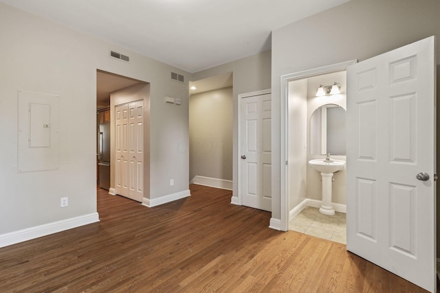 unfurnished bedroom with wood finished floors, ensuite bath, baseboards, and stainless steel refrigerator