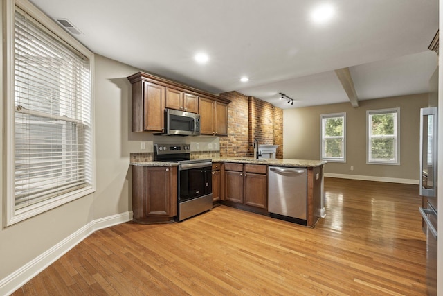 kitchen with stainless steel appliances, baseboards, a peninsula, a sink, and light wood-style floors