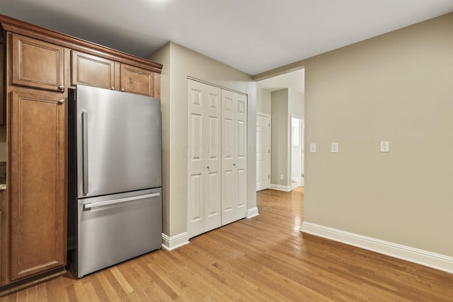 kitchen with freestanding refrigerator, light wood finished floors, baseboards, and brown cabinets
