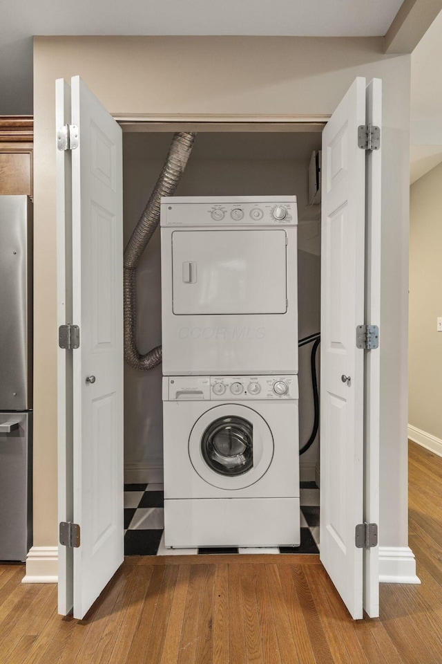 laundry area with stacked washer / dryer, wood finished floors, and baseboards