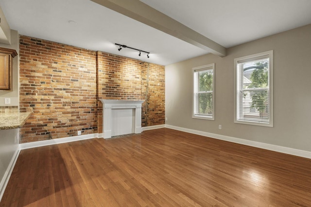 unfurnished living room with baseboards, wood finished floors, brick wall, rail lighting, and a fireplace