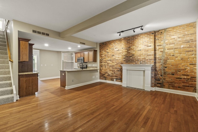 unfurnished living room featuring stairs, dark wood finished floors, baseboards, a sink, and brick wall