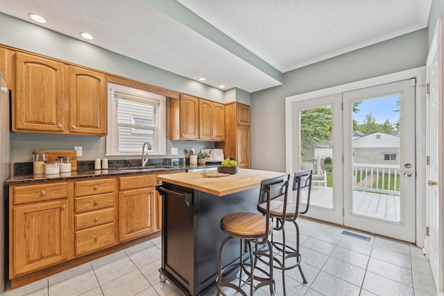 1057 Harrison Ave, Columbus, OH 43201 - kitchen featuring butcher block countertops, a kitchen bar, dishwasher, light tile patterned floors, and crown molding
