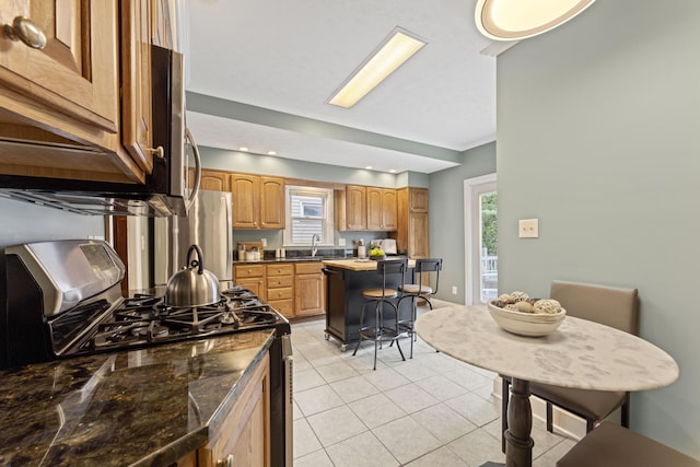 1057 Harrison Ave, Columbus, OH 43201 - kitchen with stainless steel appliances, light tile patterned floors, dark countertops, and a breakfast bar