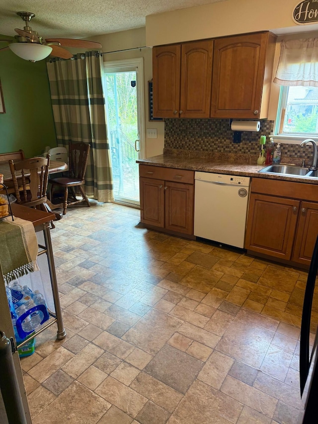 kitchen featuring white dishwasher, a sink, plenty of natural light, tasteful backsplash, and a textured ceiling