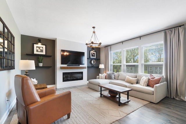 living area with light wood-style floors, a chandelier, and a glass covered fireplace