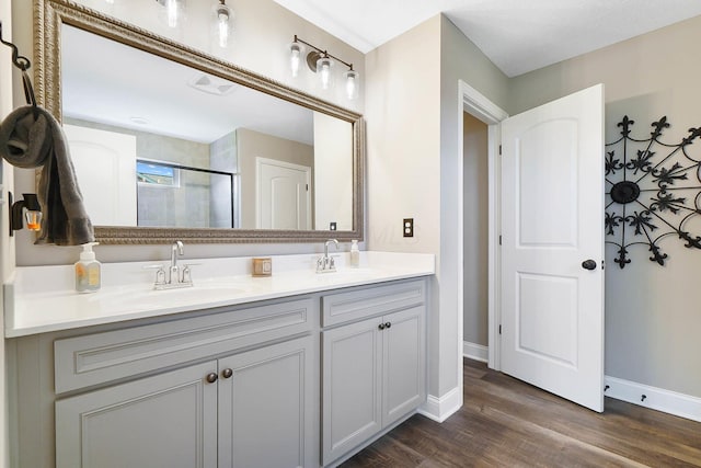 bathroom with a shower stall, wood finished floors, double vanity, and baseboards