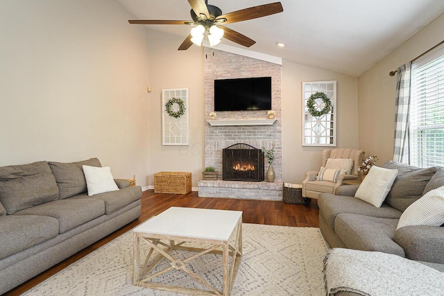 living area featuring vaulted ceiling, wood finished floors, a brick fireplace, a ceiling fan, and baseboards