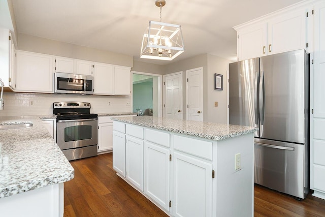 kitchen with appliances with stainless steel finishes, a chandelier, a kitchen island, backsplash, and white cabinets
