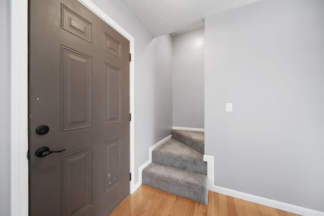 foyer entrance featuring baseboards, stairway, light wood-type flooring, and a textured ceiling