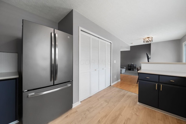 kitchen featuring freestanding refrigerator, light wood-style flooring, light countertops, a textured ceiling, and baseboards