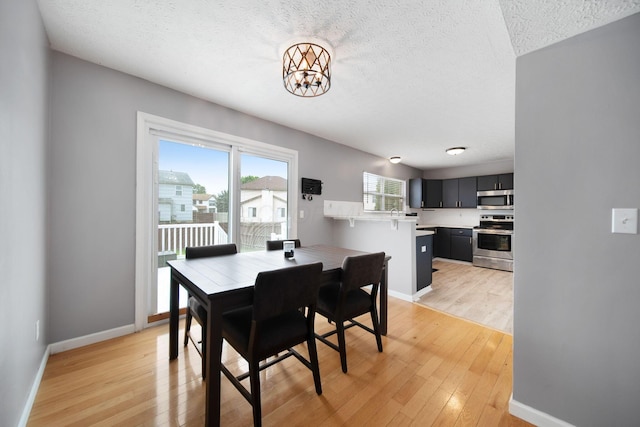 dining area featuring a chandelier, light wood-style floors, baseboards, and a textured ceiling