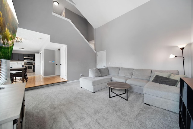 living area with high vaulted ceiling, light carpet, baseboards, and stairs
