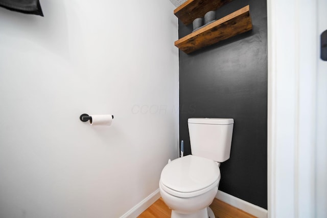 bathroom featuring baseboards, wood finished floors, and toilet