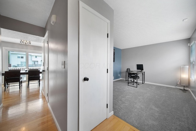 hall featuring baseboards, a desk, light wood finished floors, and a textured ceiling