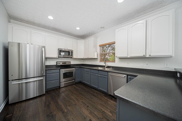 1019 Wallace Dr, Delaware, OH 43015 - kitchen featuring appliances with stainless steel finishes, a sink, dark countertops, dark wood finished floors, and a textured ceiling