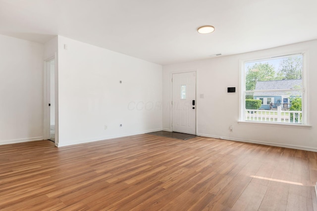 unfurnished living room with light wood finished floors, plenty of natural light, and baseboards