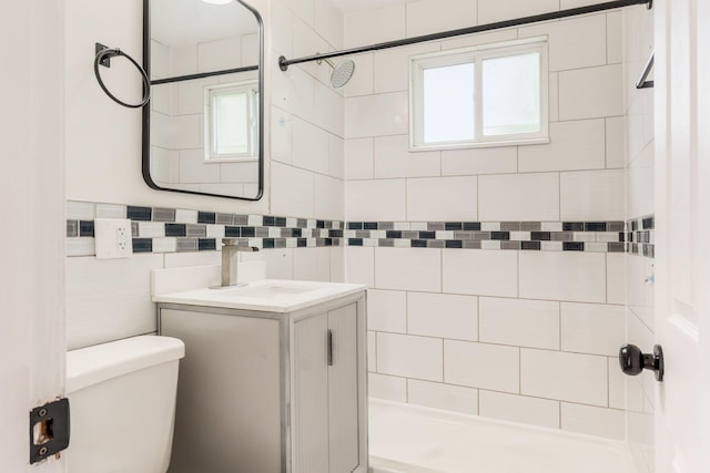 bathroom featuring tiled shower, toilet, healthy amount of natural light, vanity, and tile walls
