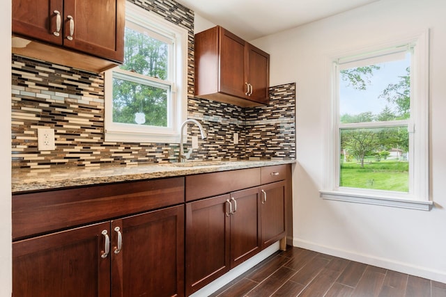 kitchen featuring a sink, baseboards, dark wood finished floors, decorative backsplash, and light stone counters