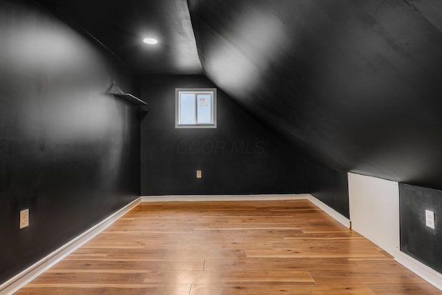 additional living space with vaulted ceiling, light wood-type flooring, and baseboards
