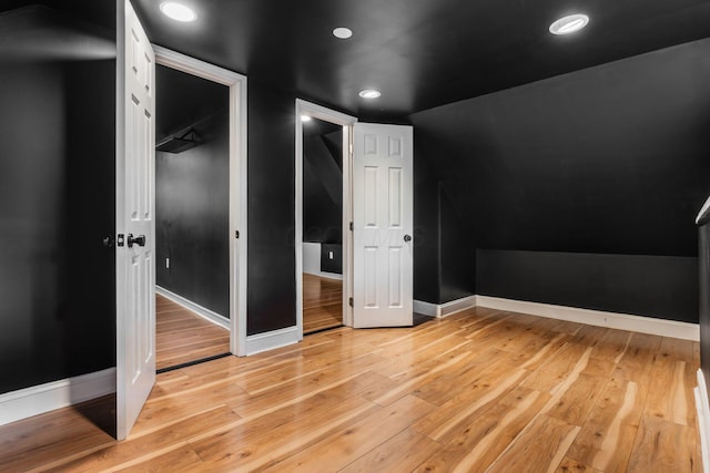 unfurnished bedroom featuring light wood-type flooring, baseboards, recessed lighting, lofted ceiling, and a closet