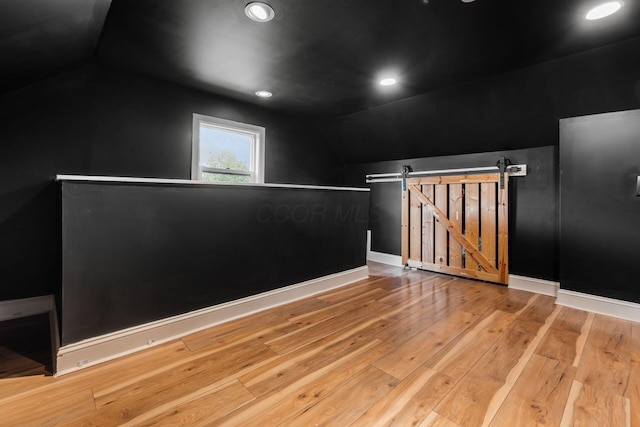 empty room with vaulted ceiling, hardwood / wood-style flooring, a barn door, baseboards, and recessed lighting