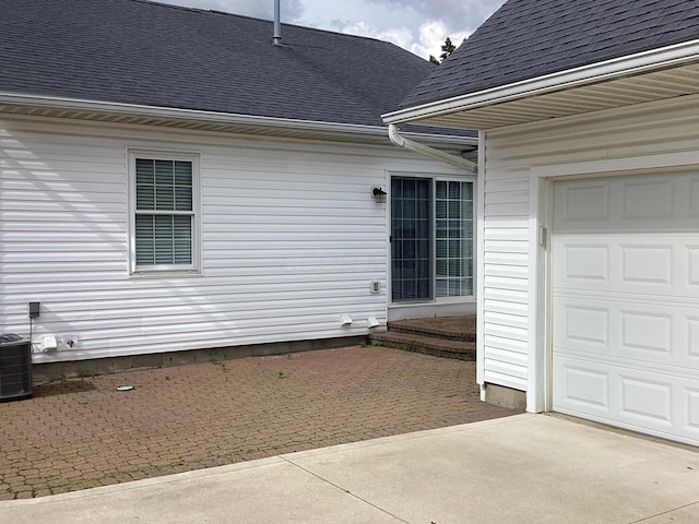 view of exterior entry with a shingled roof, driveway, and central air condition unit