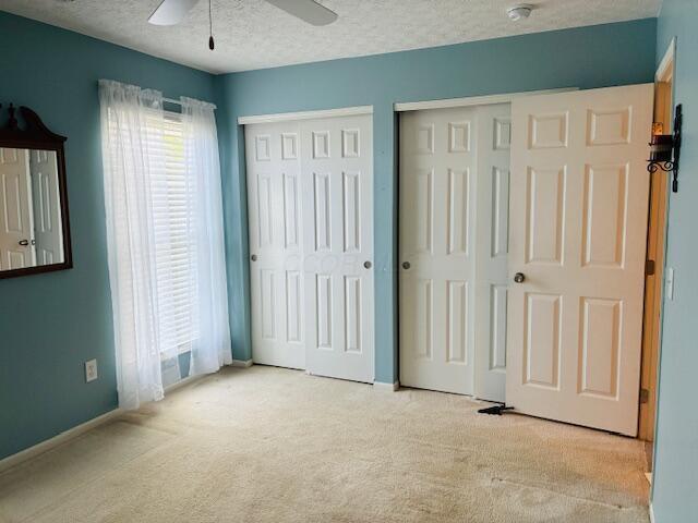 unfurnished bedroom with light colored carpet, multiple closets, baseboards, a ceiling fan, and a textured ceiling