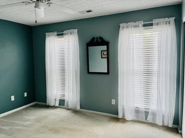 carpeted spare room with plenty of natural light, a ceiling fan, baseboards, and a textured ceiling