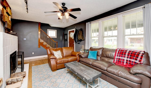 living area with ceiling fan, wood finished floors, stairway, baseboards, and a fireplace with raised hearth