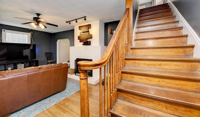 stairway featuring a ceiling fan, a fireplace, wood finished floors, track lighting, and arched walkways