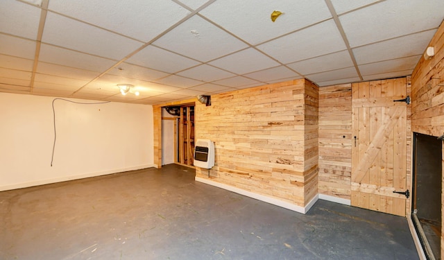 finished below grade area featuring heating unit, wood walls, a paneled ceiling, and baseboards
