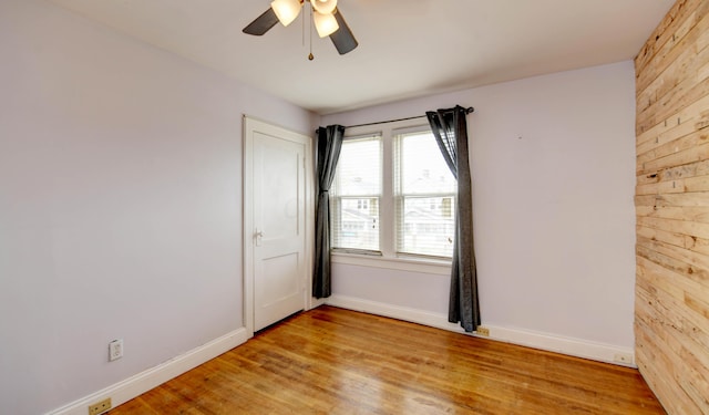 spare room with wood walls, baseboards, light wood-style floors, and ceiling fan