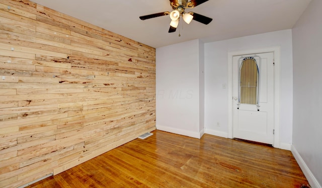 spare room featuring wooden walls, wood finished floors, a ceiling fan, and baseboards