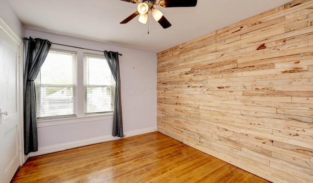 unfurnished room featuring wood walls, a ceiling fan, light wood-style flooring, and baseboards