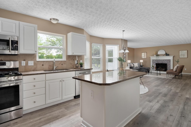 6289 Corley Dr, Dublin, OH 43016 - kitchen featuring stainless steel appliances, a sink, light wood-type flooring, a fireplace, and white cabinets