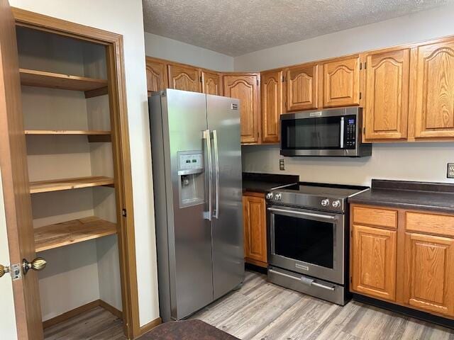 50 Stagecoach Rd, Chillicothe, OH 45601 - kitchen with stainless steel appliances, light wood-style floors, dark countertops, a textured ceiling, and brown cabinetry