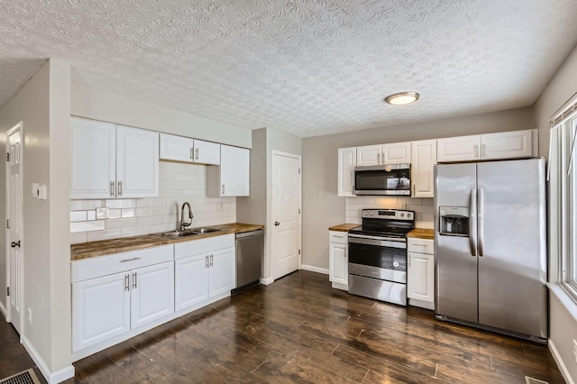 kitchen featuring appliances with stainless steel finishes, a sink, butcher block countertops, backsplash, and dark wood-type flooring