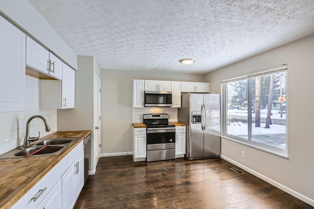 kitchen featuring stainless steel appliances, a sink, decorative backsplash, baseboards, and a textured ceiling